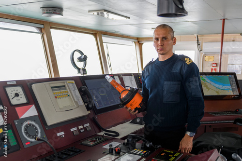 Officer on watch with EPIRB on the navigational bridge. Caucasian man in blue uniform sweater using emergency position indicating radio beacon on the bridge of cargo ship.