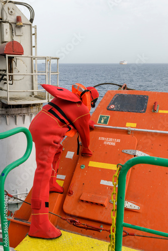 Seaman wearing Immersion Suit on Muster station. Abandon ship drill. Free fall boat. Cargo vessel. © Alexey Seafarer