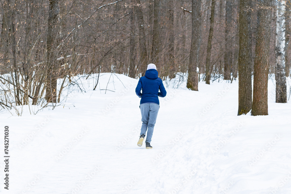 An unrecognizable young beautiful athletic girl jogs along a path in the winter forest