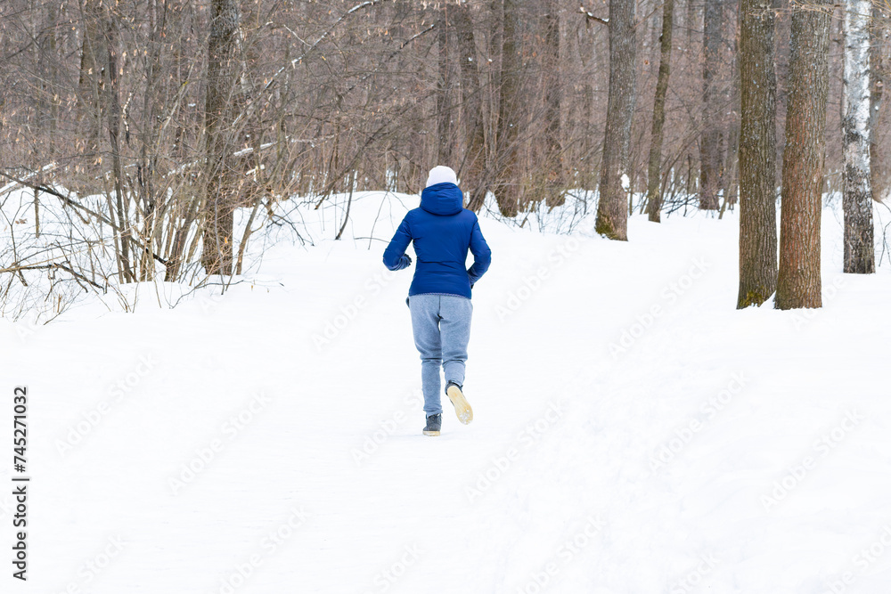 An unrecognizable young beautiful athletic girl jogs along a path in the winter forest