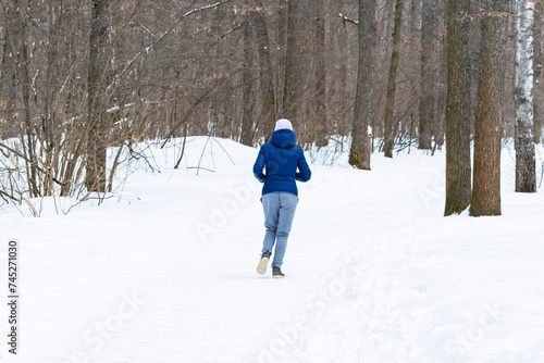An unrecognizable young beautiful athletic girl jogs along a path in the winter forest