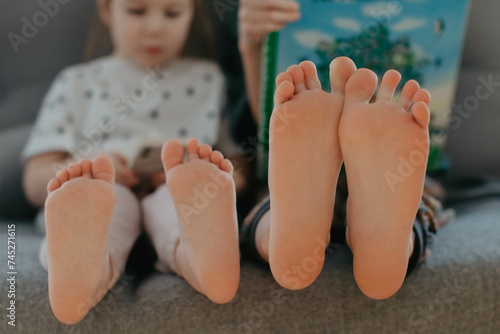 Big brother and little sister holding bare feet close up to camera . Blurred face on background 