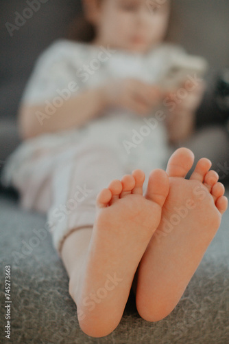 little girl holding bare feet close up to camera and reading book . Blurred face on background 