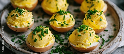 A plate of deviled eggs topped with fresh chives, presenting a delicious and visually appealing appetizer option. The eggs are filled with a creamy and flavorful mixture and garnished with finely photo