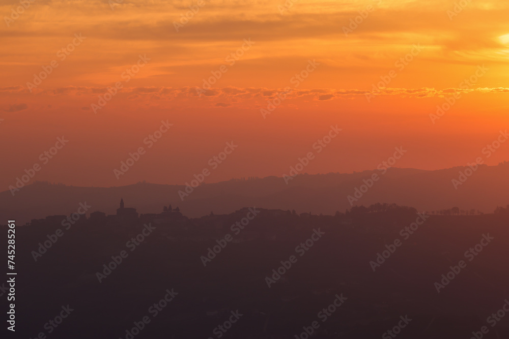 Fototapeta premium pink sunrise sky with the silhouette of an italian village on the top of a hill in Piedmont