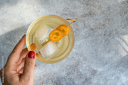 Overhead view of a woman reaching for a vodka tonic cocktail with kumquat garnish photo