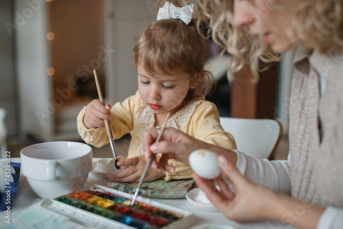 Close-up of a mother and daughter sitting at a dining table decorating Easter eggs photo