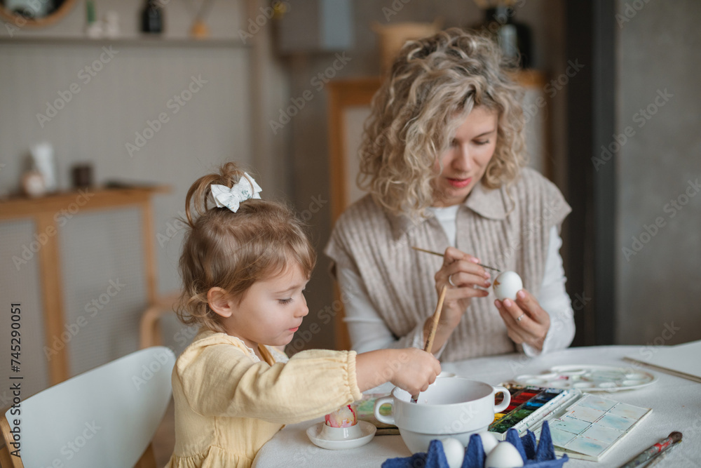 Close-up of a mother and daughter sitting at a dining table decorating Easter eggs Close-up of a mother and daughter sitting at a dining table decorating Easter eggs