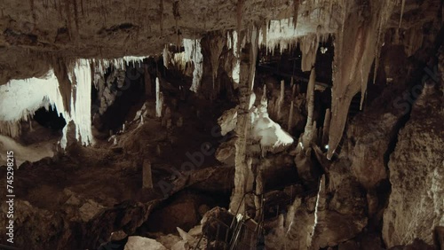 Interior of a vast limestone cave is adorned with geological formations including stalactites hanging from the ceiling and stalagmites rising from the ground photo