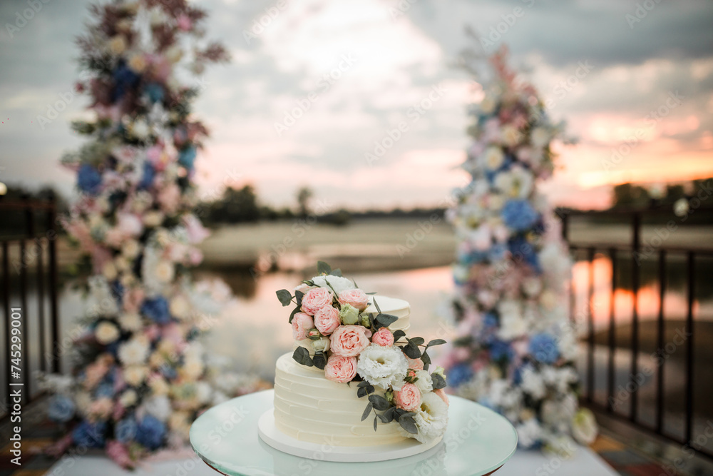 wedding cake decorated with roses at sunset near the water