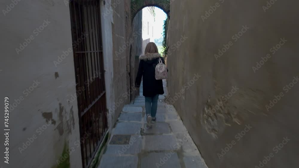 A female tourist strolls down a very narrow street with a medieval stone arch, Caceres, Extremadura A female tourist strolls down a very narrow street with a medieval stone arch, Caceres, Extremadura