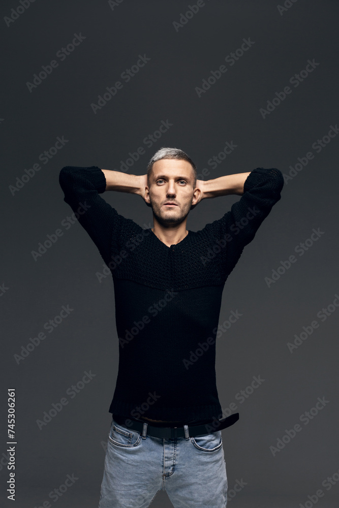 A young man in a black jumper and jeans stands on a gray background. A young man in a black jumper and jeans stands on a gray background.
