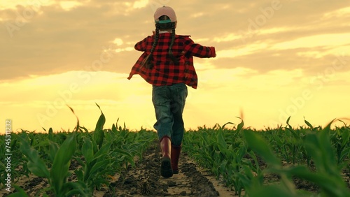 Child runs in rubber boots on field with sprouts. Happy little girl rubber boots run on field sunset. Farmer child run in field corn sprouts. Happy carefree childhood. Growing corn, agricultural, food