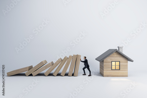 A conceptual image of a man preventing a falling row of dominoes from crashing into a small house, symbolizing protection and security photo