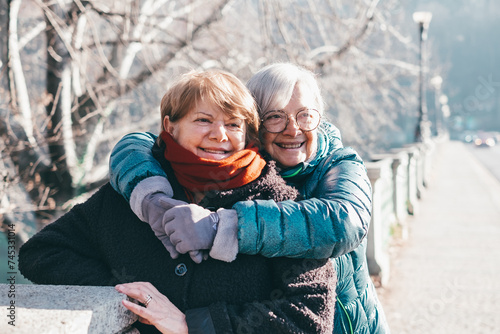 Happy couple of elderly women meet and embrace each other in the park, two senior friends or family members stay together expressing love and tenderness