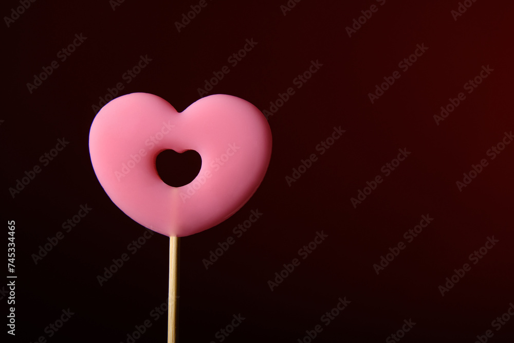 Pink heart-shaped lollipop on a dark red background. The word is love. Horizontal banner for Valentine's Day.