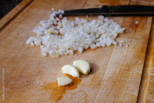 Garlic cloves and chopped onion on a wooden cutting board ready to cook. Fresh vegetable ingredients. Cooking at home. Healthy eating. Homemade food preparation. Vegetarian or vegan diet.