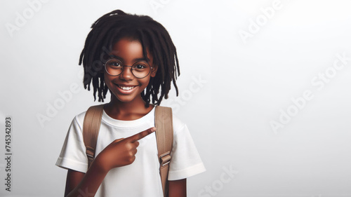 Adorable child 10 years old with a backpack, in a white T-shirt and glasses, pointing towards an empty space, white background