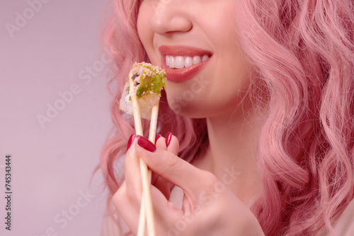 Young woman with red nails and pink hair is eating sushi.