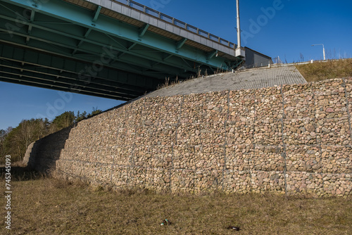 engineering structure made of stones behind metal wire netting to strengthen the river bank near the road bridge