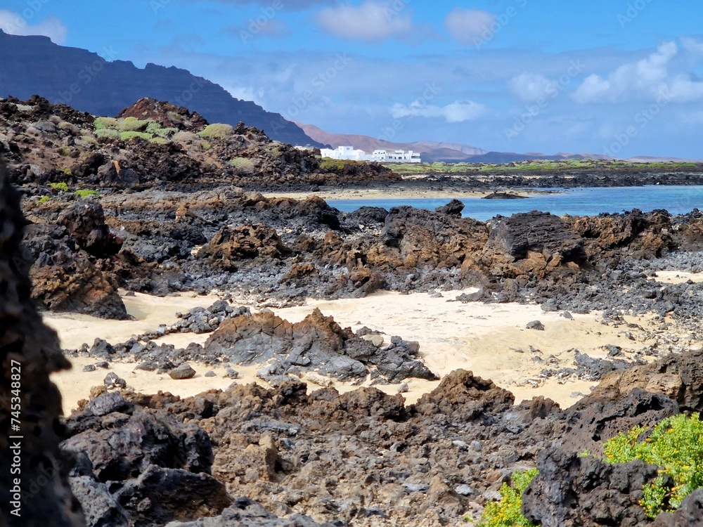 Contrast of black volcanic rock, white sand, white building and blue sea