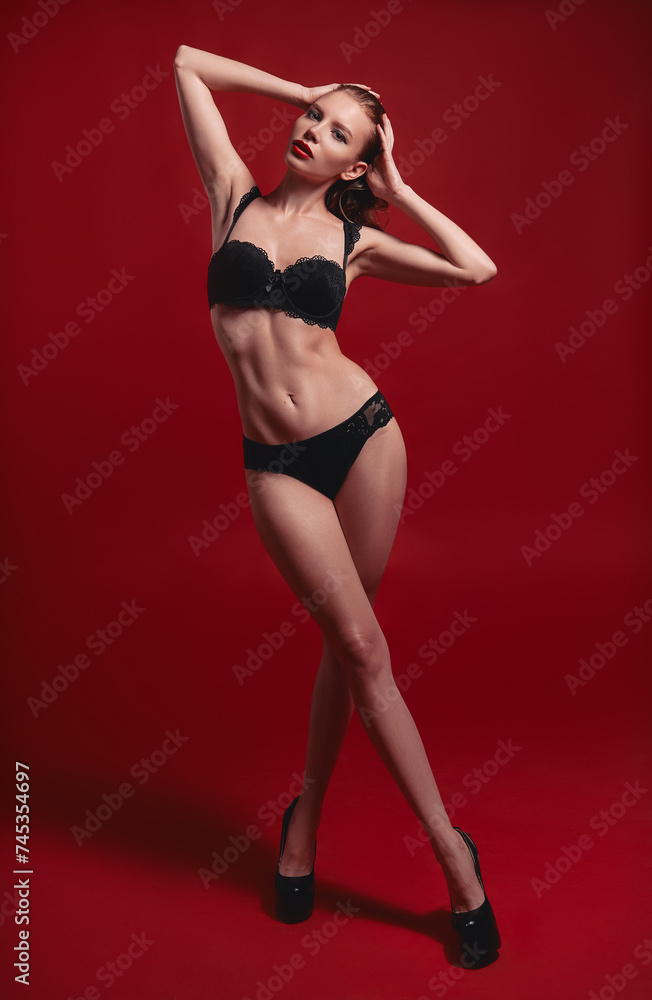 Studio fashion shot of sexy sweet young woman. Portrait of beautiful seductive girl dressed in black lingerie. Sensual graceful lady against deep red background