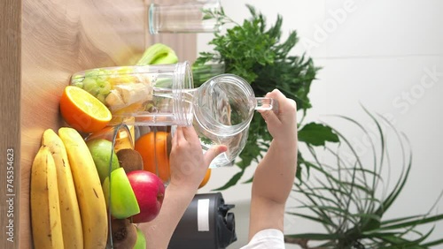 Little girl prepares fresh organic fruit smoothie. A girl pours water into a blender with fruit and makes a healthy fruit smoothie. Vegetarian, clean diet, healthy lifestyle concept photo