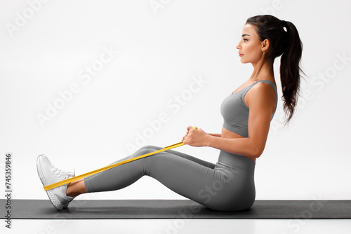 Athletic girl doing resistance band exercise for back on gray background. Fitness woman working out