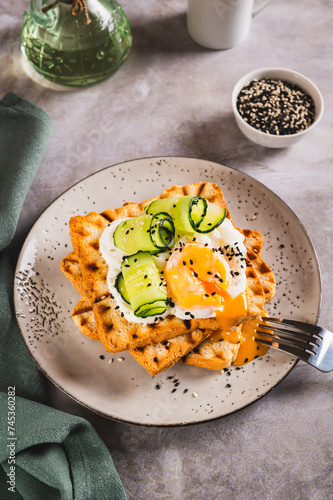 Waffles with poached egg, cucumber and sour cream on a plate on the table vertical view