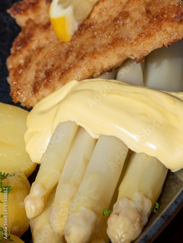 Close-up of a Wiener-style pork schnitzel with white asparagus, jacket potatoes and hollandaise sauce