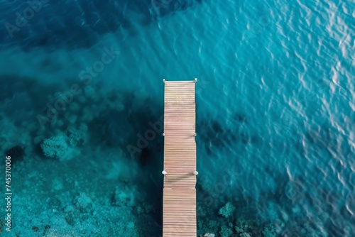 Aerial View of Pier and Sea - An aerial perspective shows a wooden pier stretching into the vibrant blue of a peaceful sea, surrounded by nature. © Tida