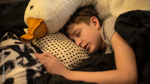 Quadro em tela a boy is sleeping in the bed with his large soft toy goose