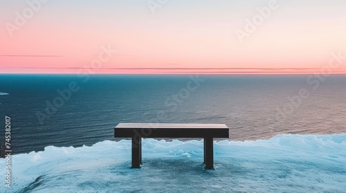 a bench sitting on top of a pile of snow next to the ocean with a pink sky in the background. photo