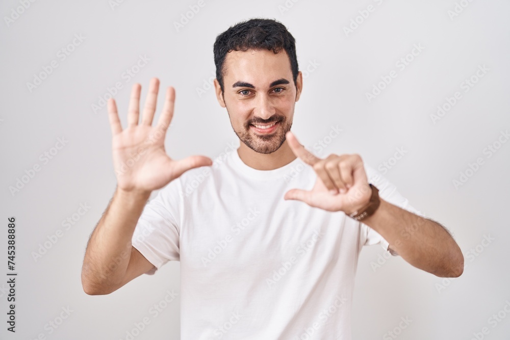 Handsome hispanic man standing over white background showing and pointing up with fingers number seven while smiling confident and happy. Handsome hispanic man standing over white background showing and pointing up with fingers number seven while smiling confident and happy.