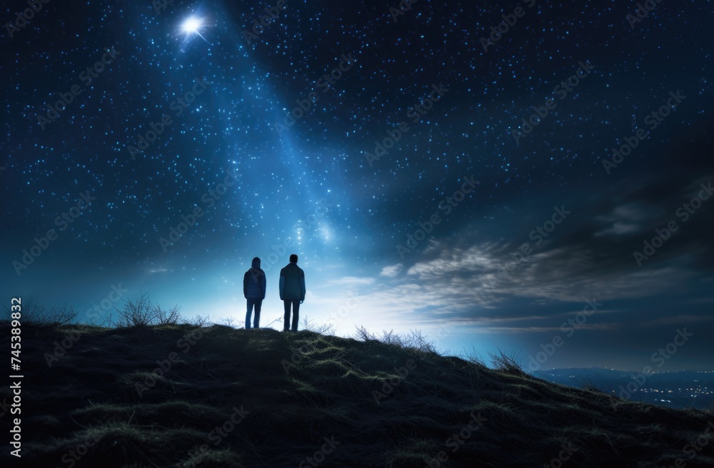 Two people standing on top of a hill at night.