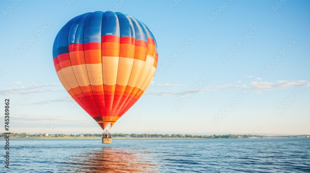 Fototapeta premium a colorful hot air balloon flying over a body of water with a blue sky and some clouds in the background.