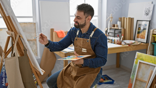 Fotografi Happy young hispanic man drawing with confidence, art studioâ€™s resident artist