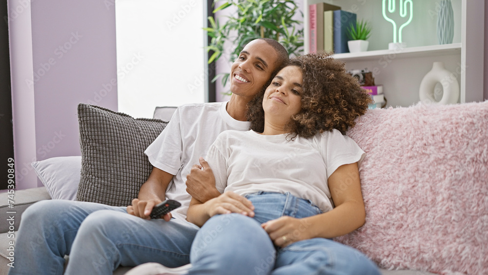 Beautiful couple joyfully watching their favorite film, sitting on the couch at home, sharing smiles and a laugh