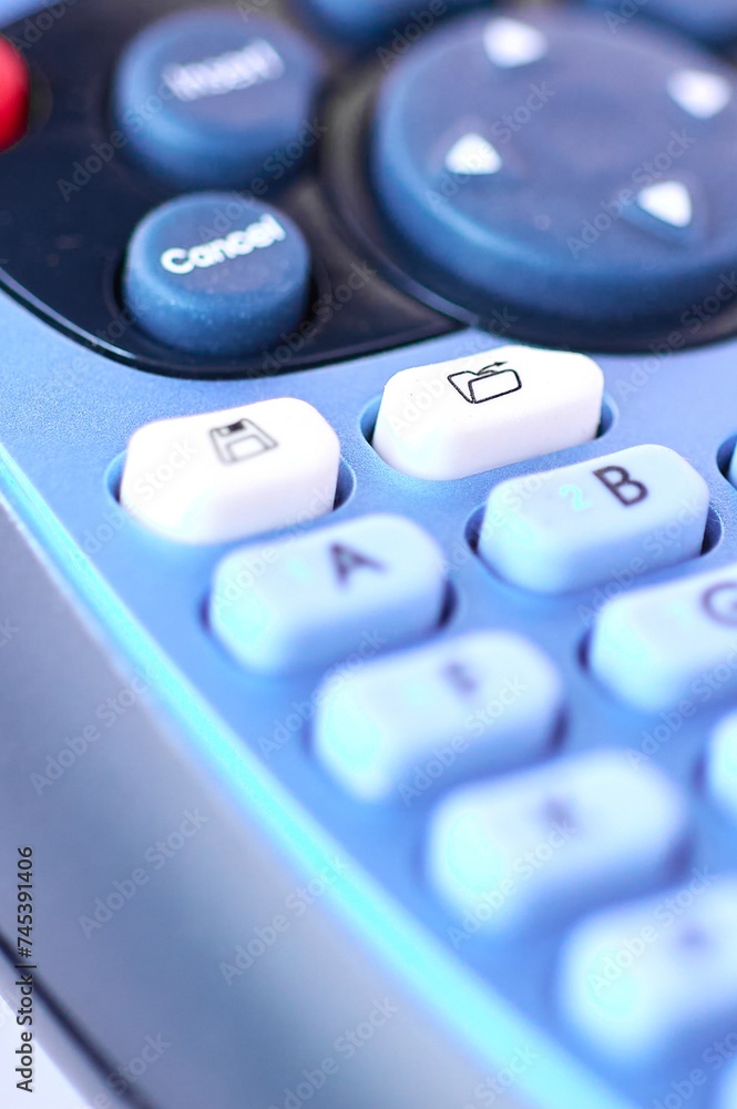 Detailed image of a blue electronic labeling machine for thermal printing ribbon, focusing on the file folder key and everything around it out of focus. Detailed image of a blue electronic labeling machine for thermal printing ribbon, focusing on the file folder key and everything around it out of focus.