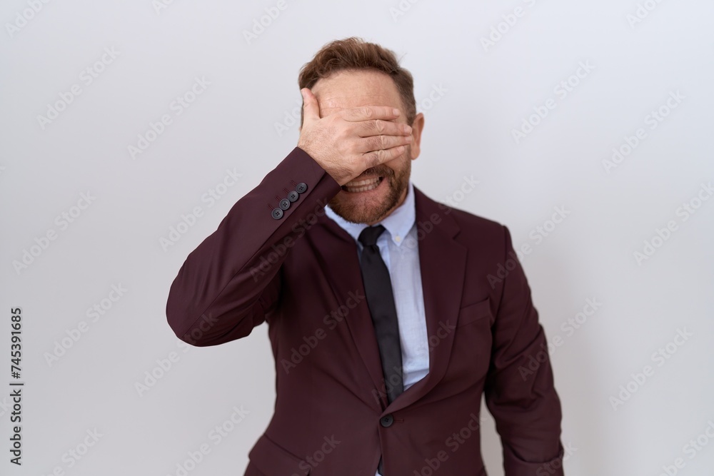 Middle age business man with beard wearing suit and tie smiling and laughing with hand on face covering eyes for surprise. blind concept. Middle age business man with beard wearing suit and tie smiling and laughing with hand on face covering eyes for surprise. blind concept.