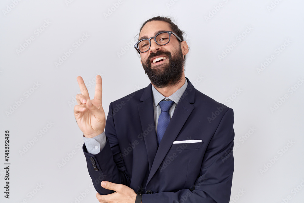 Hispanic man with beard wearing suit and tie smiling with happy face winking at the camera doing victory sign. number two. Hispanic man with beard wearing suit and tie smiling with happy face winking at the camera doing victory sign. number two.