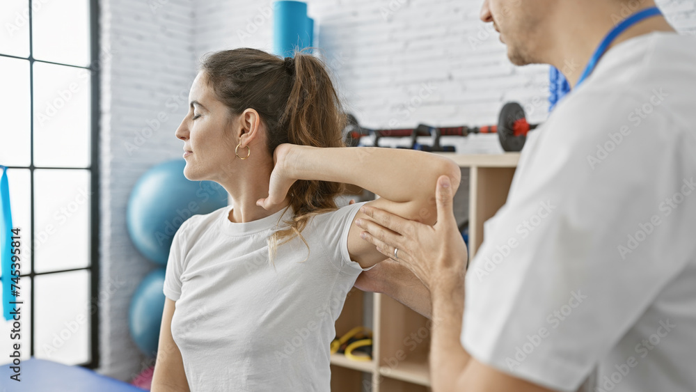 A woman receives shoulder therapy from a male physiotherapist in a modern clinic A woman receives shoulder therapy from a male physiotherapist in a modern clinic