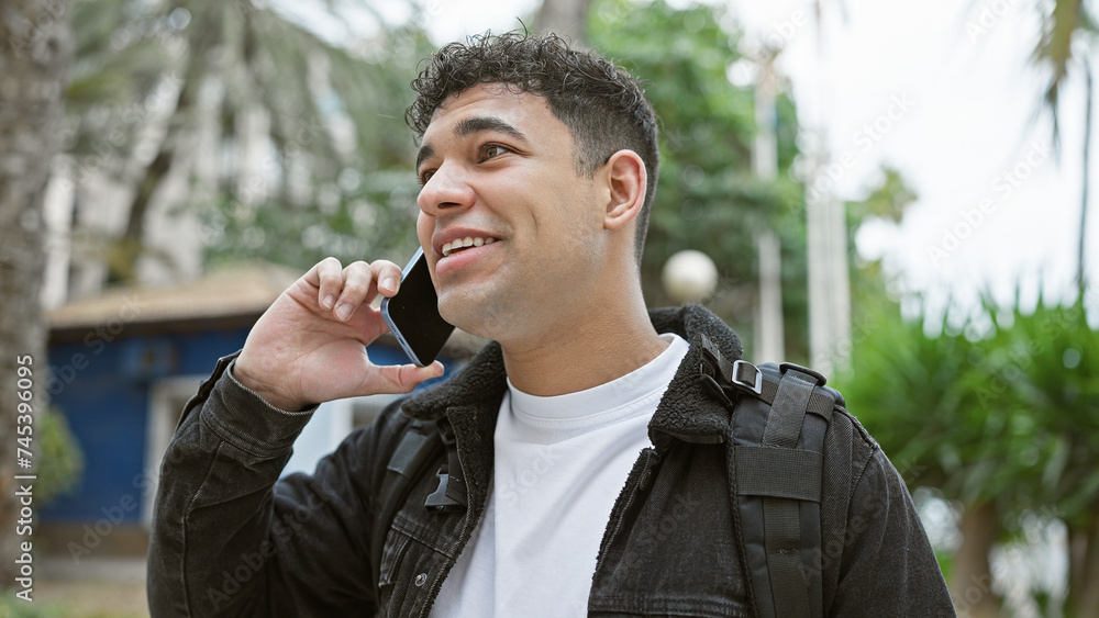A handsome man with a backpack smiling while talking on a mobile phone on a city street. A handsome man with a backpack smiling while talking on a mobile phone on a city street.