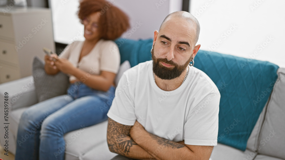 Beautiful couple looking upset while sitting together at home, girlfriend engrossed in smartphone usage Beautiful couple looking upset while sitting together at home, girlfriend engrossed in smartphone usage