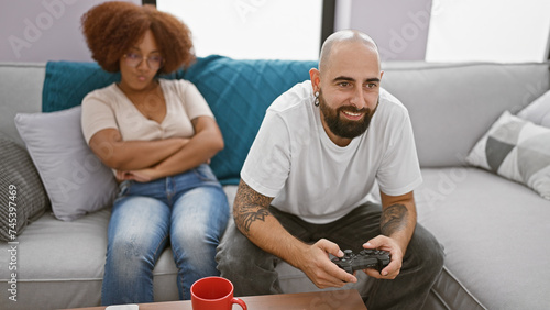 Upset beautiful couple sitting together at home, boyfriend engrossed in video game play leaves girlfriend looking concerned