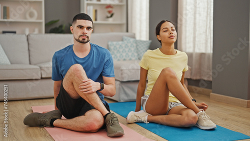 Beautiful couple in sportswear, sitting on living room floor, stretching legs together in calm yoga exercise for healthy, athletic lifestyle at home
