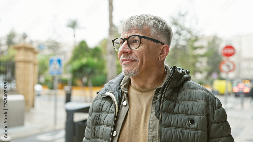 Middle-aged man with grey hair and glasses smiling outdoors on an urban street. Middle-aged man with grey hair and glasses smiling outdoors on an urban street.