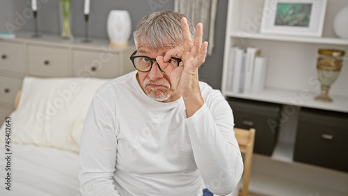 A contemplative senior man with gray hair makes a gesture while sitting in a modern bedroom. © Krakenimages.com