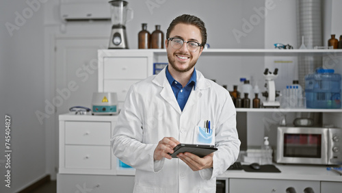 Young hispanic man scientist using touchpad smiling at laboratory