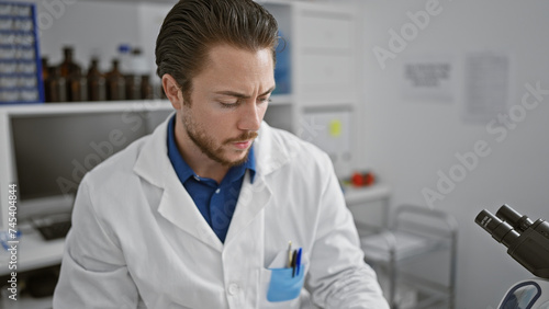 Young hispanic man scientist sitting on chair relaxed at laboratory